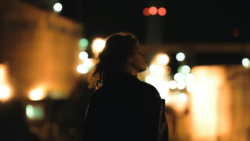 A woman standing outdoors at night with city lights blurred in the background.