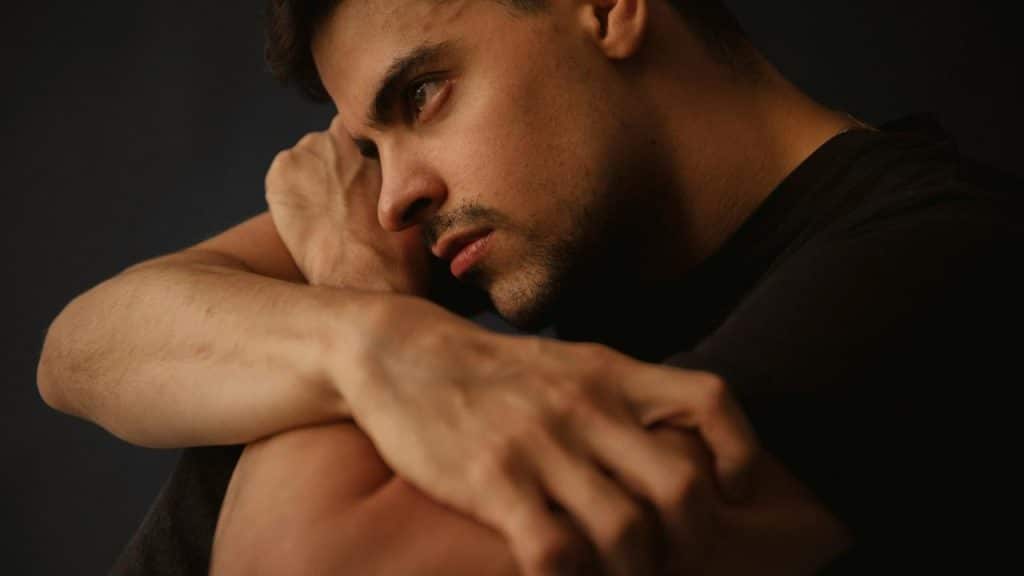 A man sitting with arms wrapped around himself looking deep in thought.