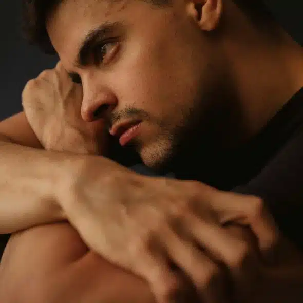 A man sitting with arms wrapped around himself looking deep in thought.