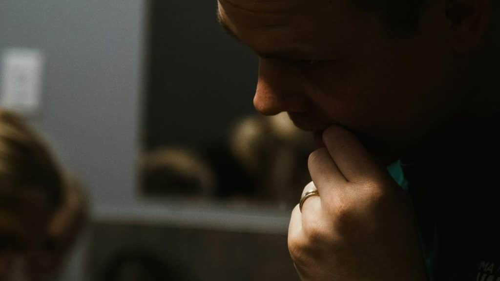 A man wearing a wedding ring touching his mouth with a thoughtful expression.