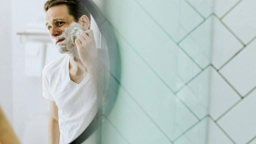 A man applying shaving cream to his face while looking in the mirror.