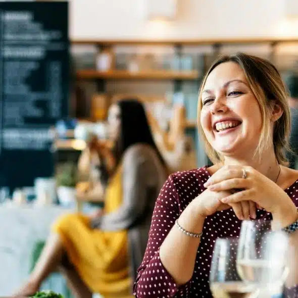 A smiling woman sitting at a café table with drinks.