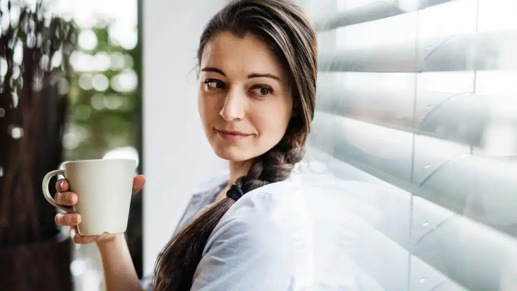 A woman holding a mug while looking out a window.