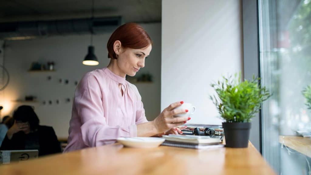 A woman in a café holding a cup while sitting by the window.