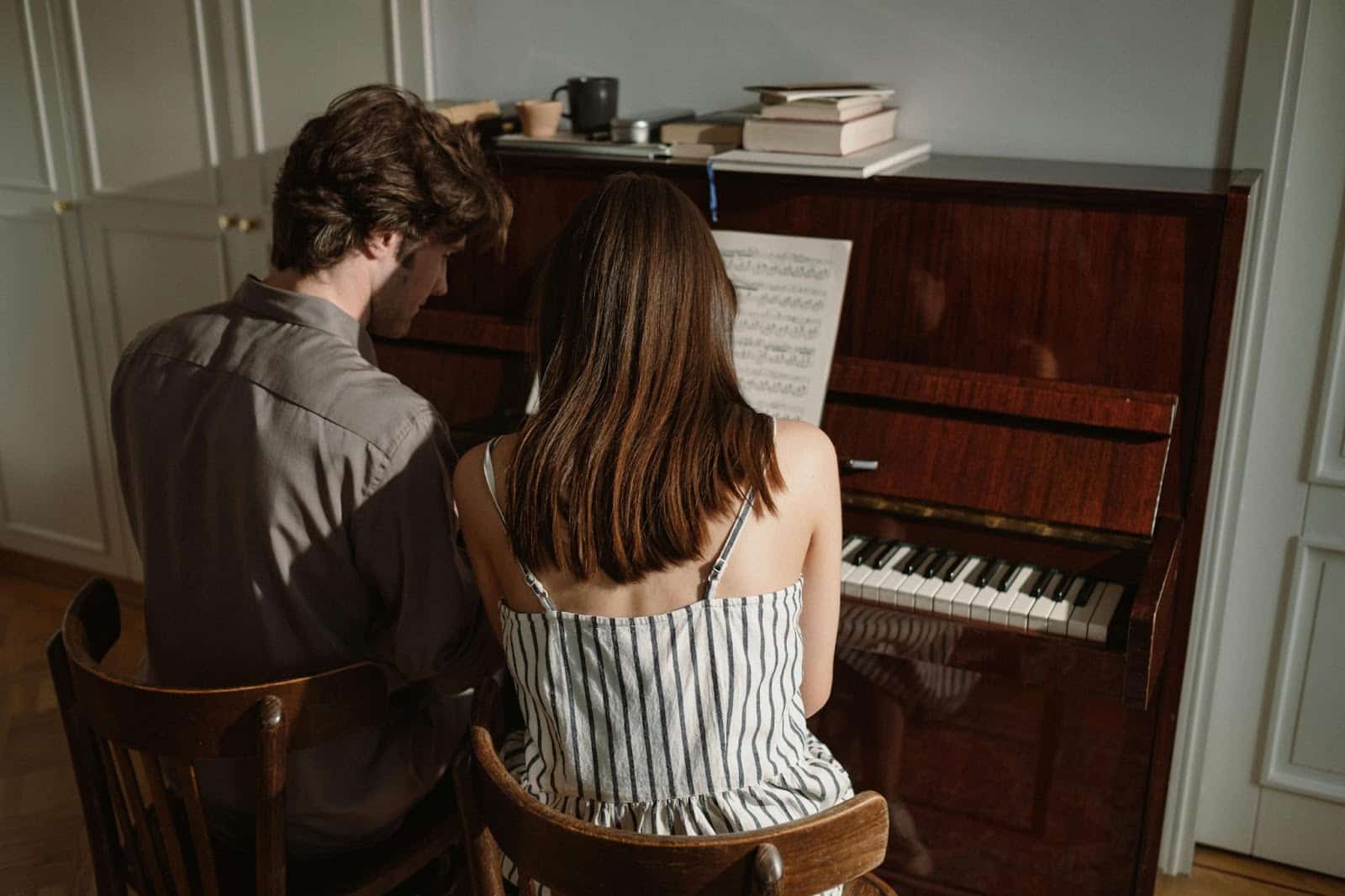 A woman teaching a man how to play piano.