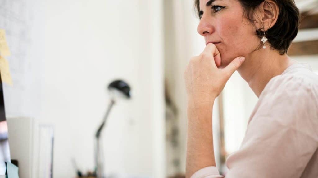 A woman sitting at a desk looking thoughtfully at a screen.