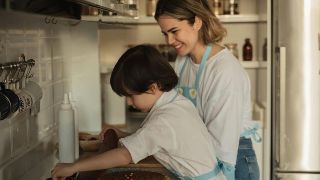 A woman and child wearing aprons baking together in a kitchen.