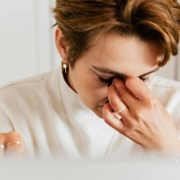 A woman in a white sweater pinching the bridge of her nose in frustration.