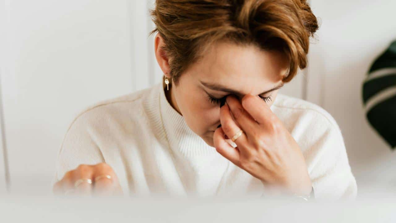 A woman in a white sweater pinching the bridge of her nose in frustration.