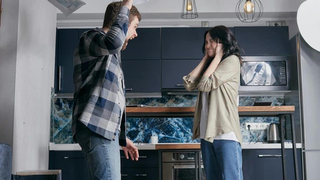 A man angrily raising papers while a woman covers her ears in distress.