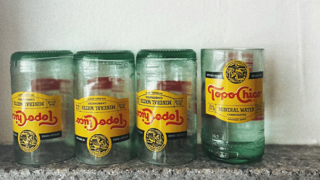 Four Topo Chico glass bottles, with three cut to be reused as drinking glasses.