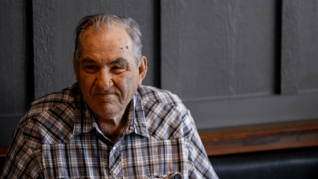 A thoughtful older man in a blue plaid shirt is looking away from the camera.