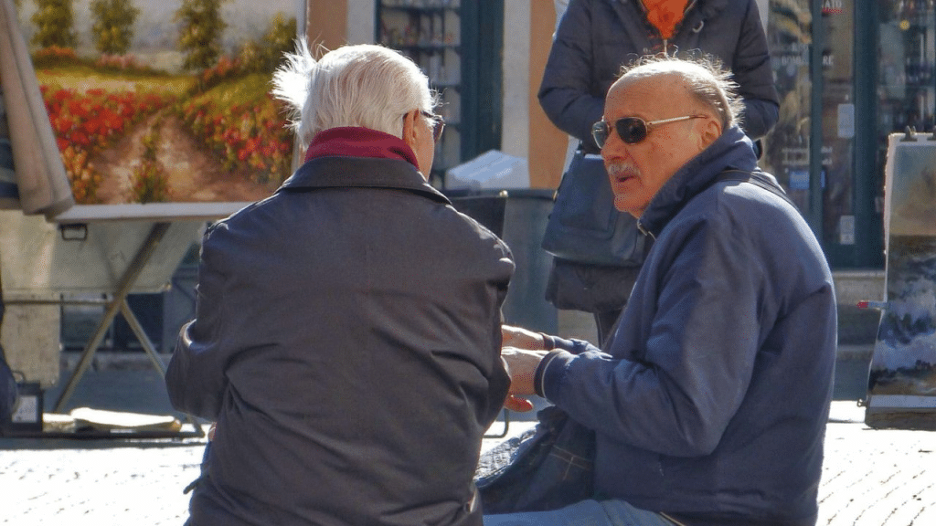 An older man is seated and looking at someone with a serious expression.