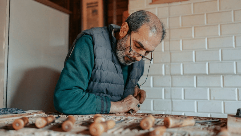 A focused man carves intricate patterns on wood in a workshop.