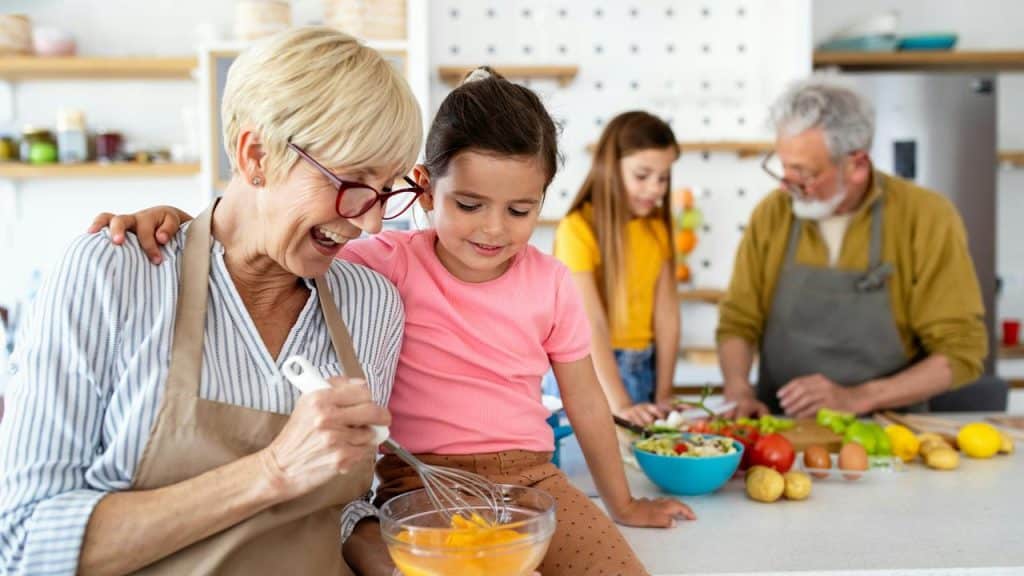 An elderly couple cooking with their grandchildren in the kitchen.
