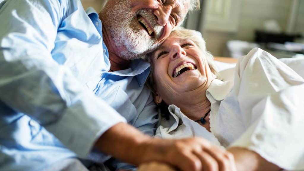 An elderly couple lying together and laughing joyfully.