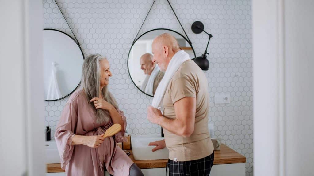 An elderly couple smiling and chatting together in the bathroom.