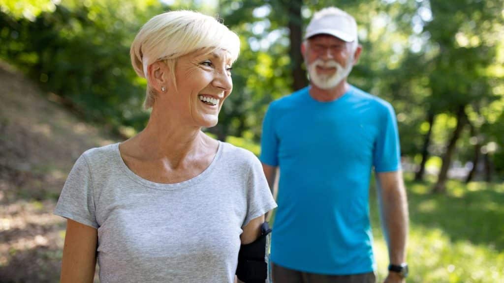 An elderly couple smiling while exercising outdoors.