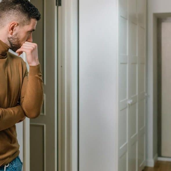 A man stands in a hallway watching a woman leave through the door.