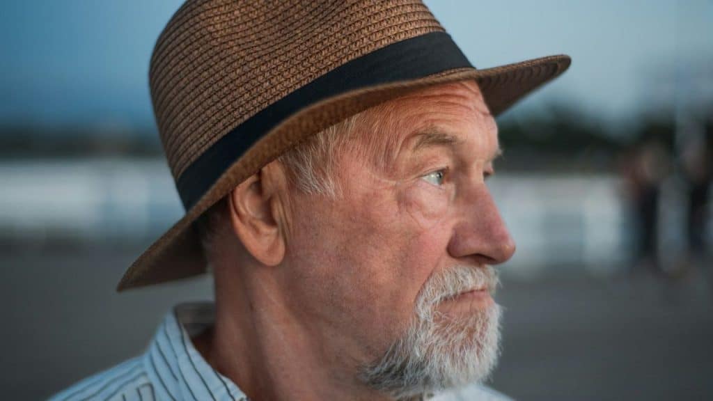 A close-up of a senior man wearing a straw hat, looking off to the side.