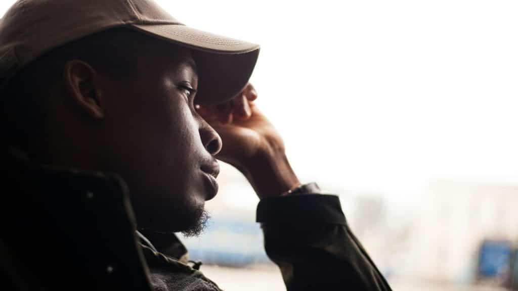 A man wearing a cap looking thoughtful while resting his head on his hand.
