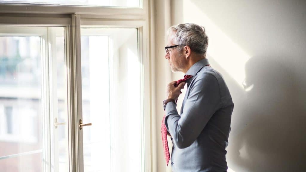 A man standing by a window adjusting his tie.