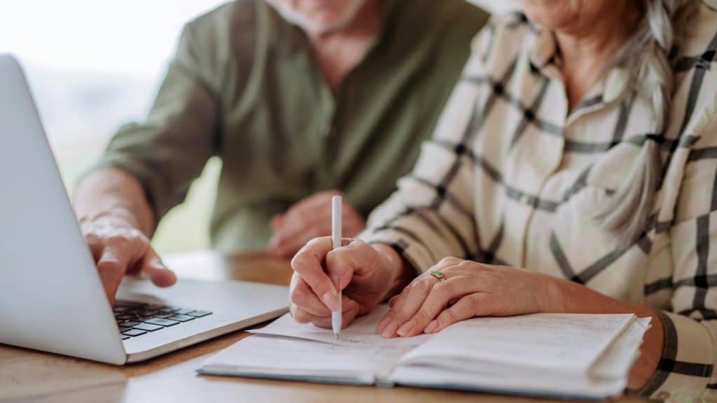 An older couple working together with a notebook and laptop.