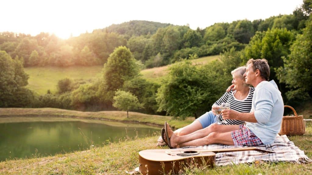 An older couple having a picnic by a lake at sunset.