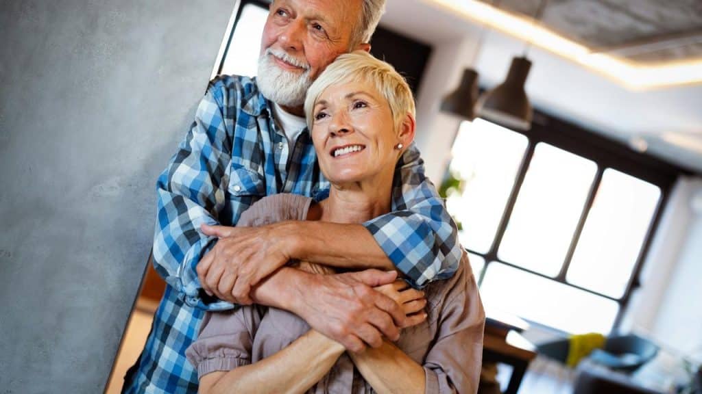 An older couple embracing and smiling together indoors.