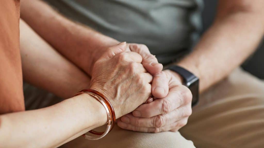An older couple holding hands closely.