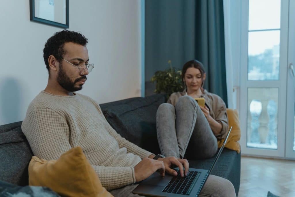 A man and woman sitting at the couch using their own gadgets