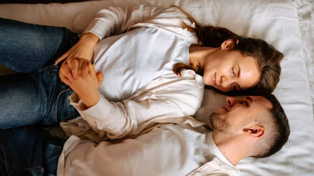 Husband placing hand gently on wife’s stomach as they lay on bed together