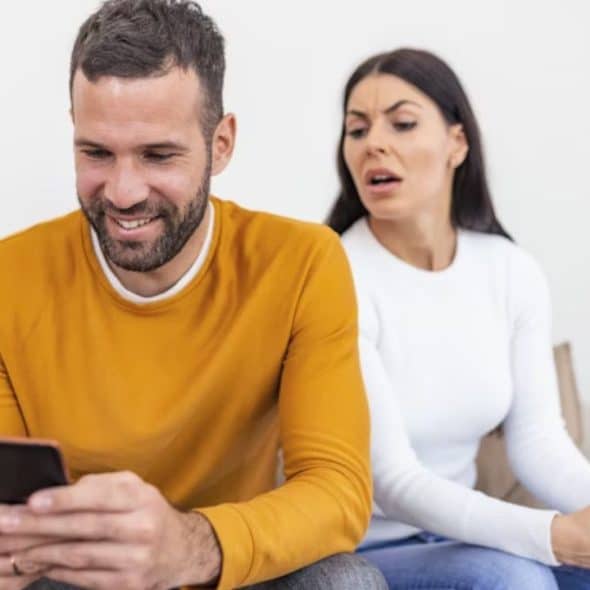 Husband ignoring wife while scrolling on his phone, wife looking disappointed