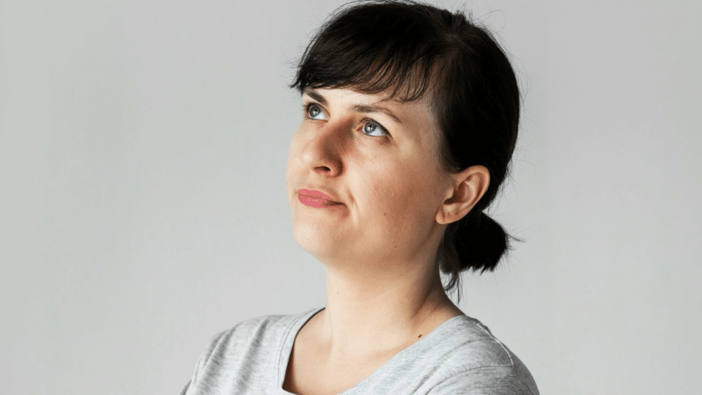 A brunette woman with blue eyes looks up and to the right.