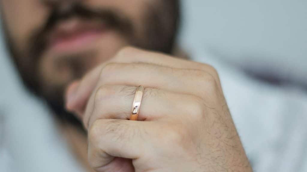 Close-up of a man's hand wearing a simple rose-gold wedding band.