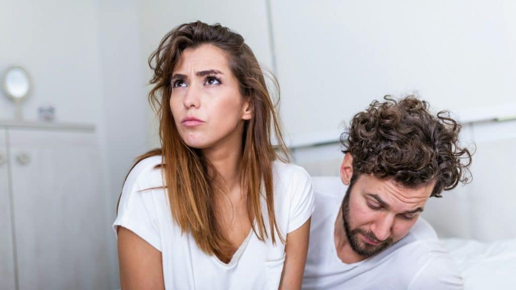 Woman looking away with a pained expression; man looks downcast next to her.