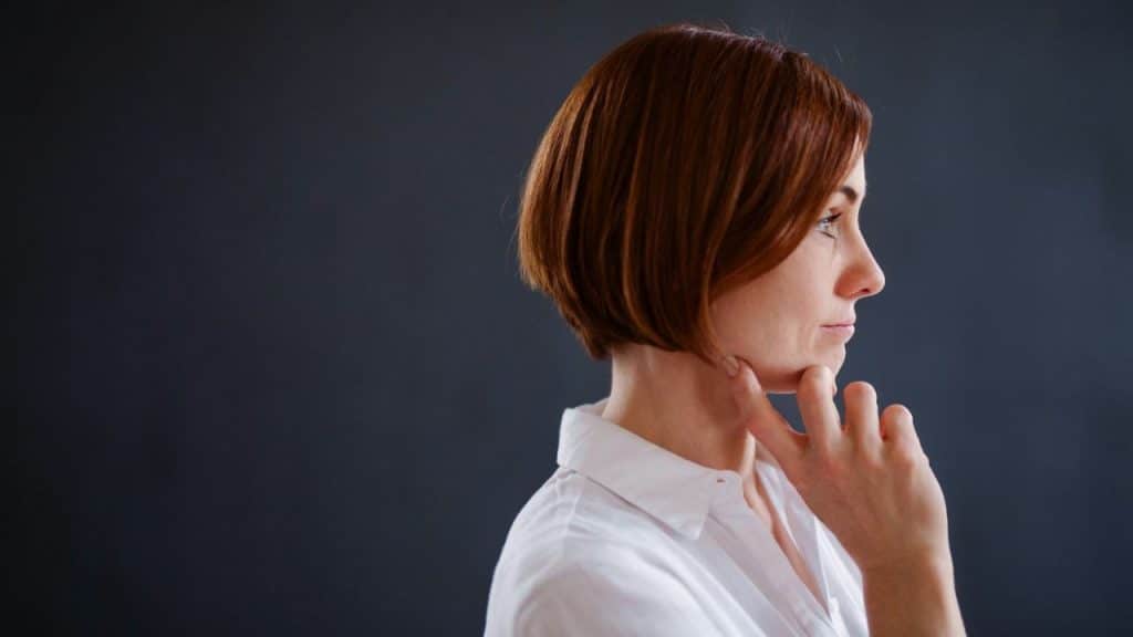 Woman with a bob haircut in a white shirt, in profile, holding her chin.