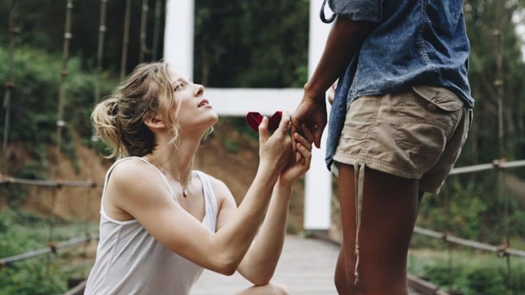 A woman holding an engagement ring box while proposing to her partner