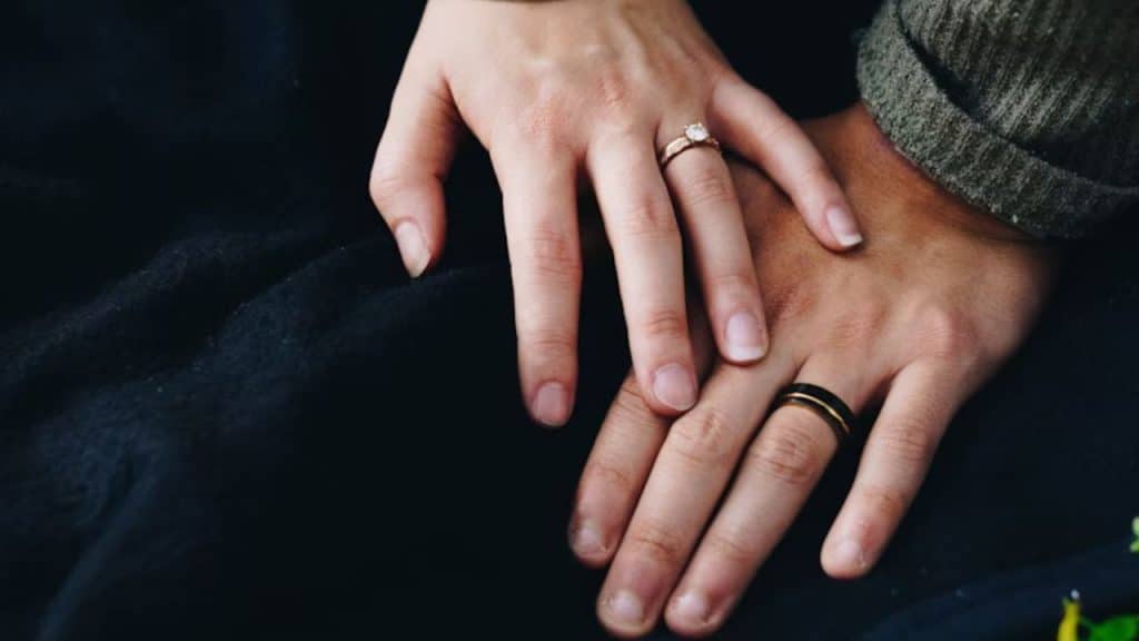 A couple sitting together, holding hands with engagement rings visible