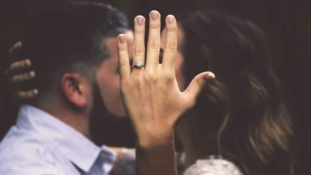 A couple kissing while showing a hand with an engagement ring