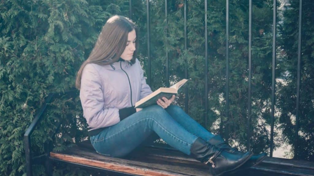 A woman reading a book at a park bench
