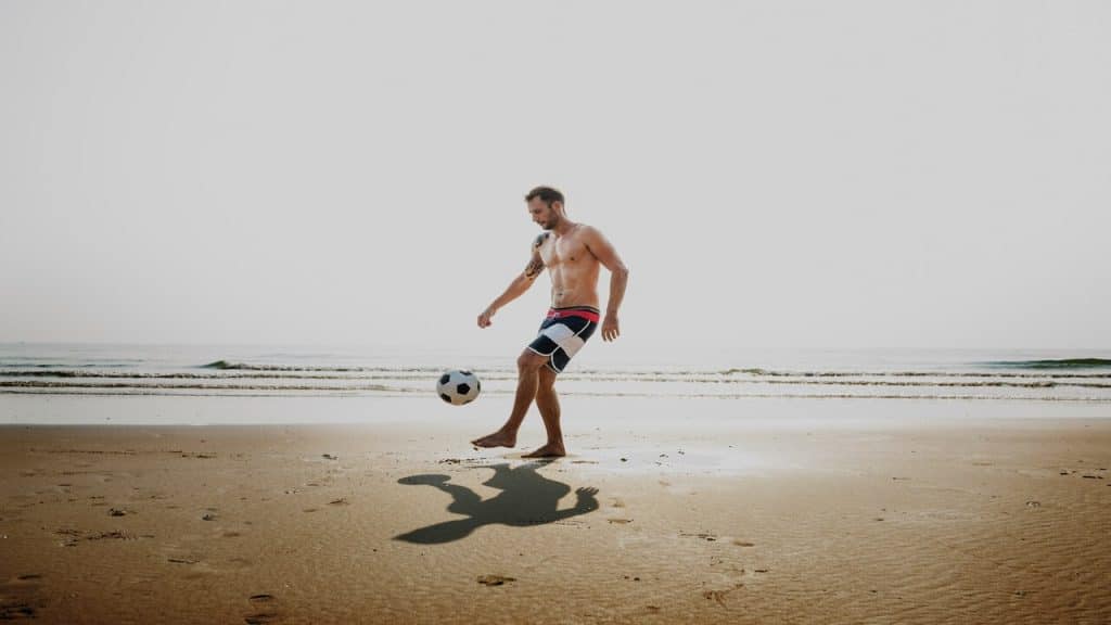A man playing soccer on the beach.