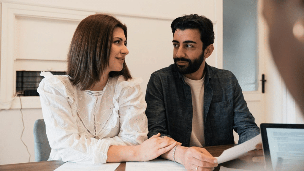 A smiling couple looks at each other while sitting at a table with papers.