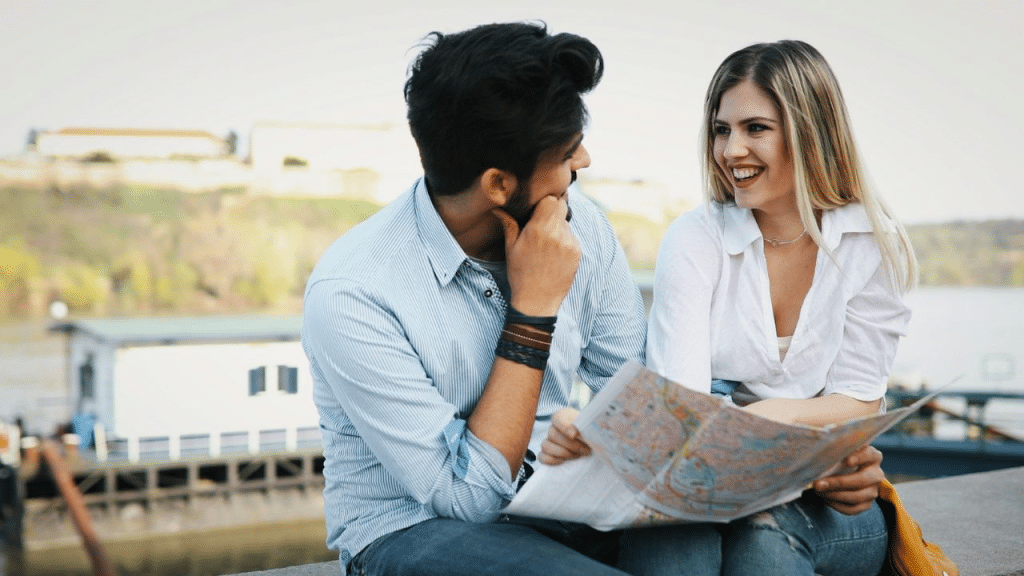 A happy couple sits together, looking at a map and talking outdoors.