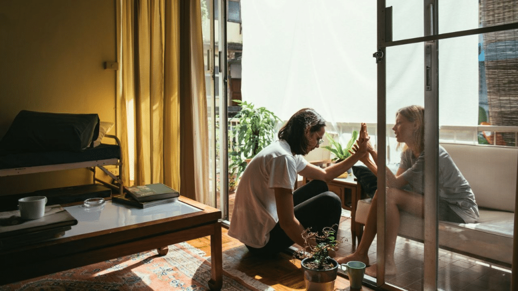 A couple touches hands through a glass door separating two rooms.