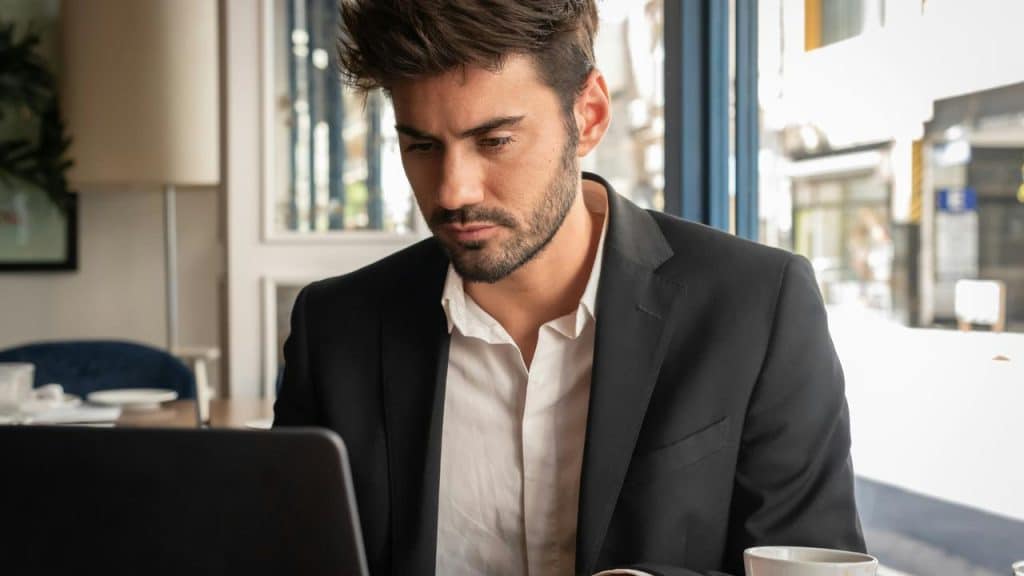 A man in a black suit working on a laptop at a café table.