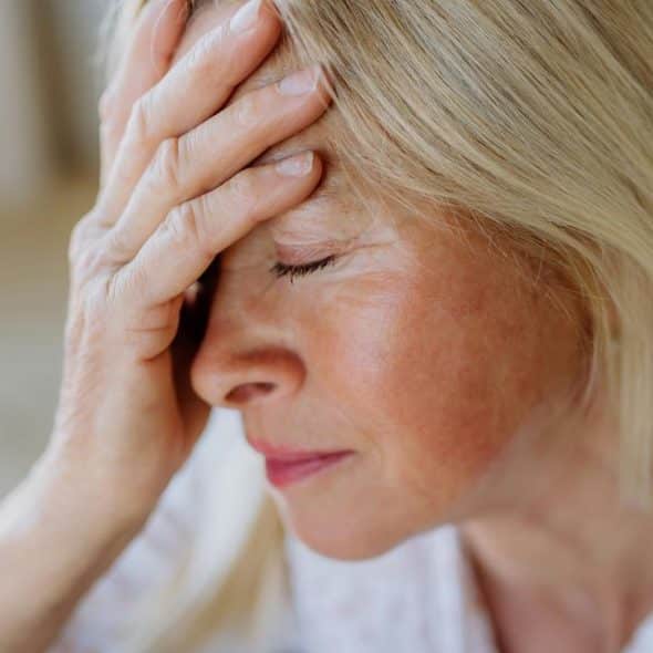 A woman with closed eyes holding her forehead in distress.