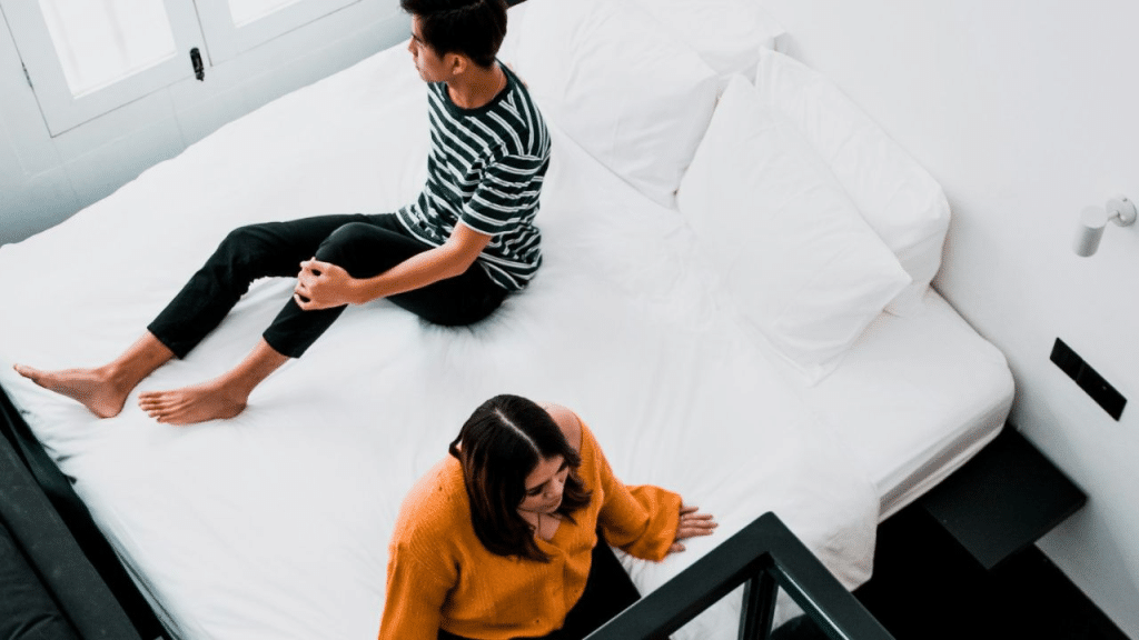 A high-angle view of a couple sitting separately on a bed.