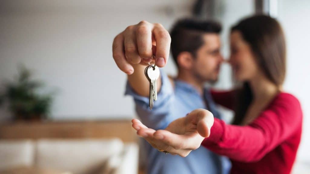 A blurred couple stands together as a man holds a house key set.