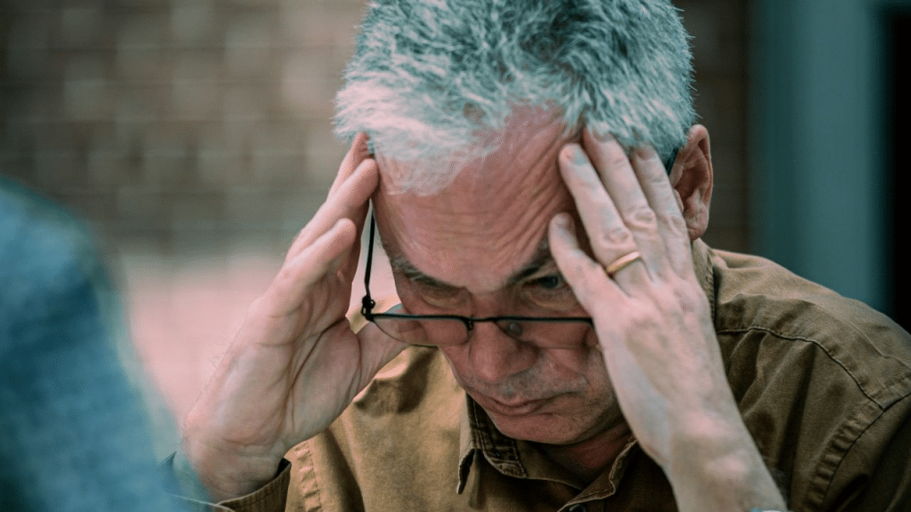 A frustrated man holds his head in his hands, looking down.